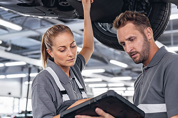 BMW Service – Werkstattteam Zwei BMW Servicetechniker mit einem Tablet unter einem angehobenen Fahrzeug.