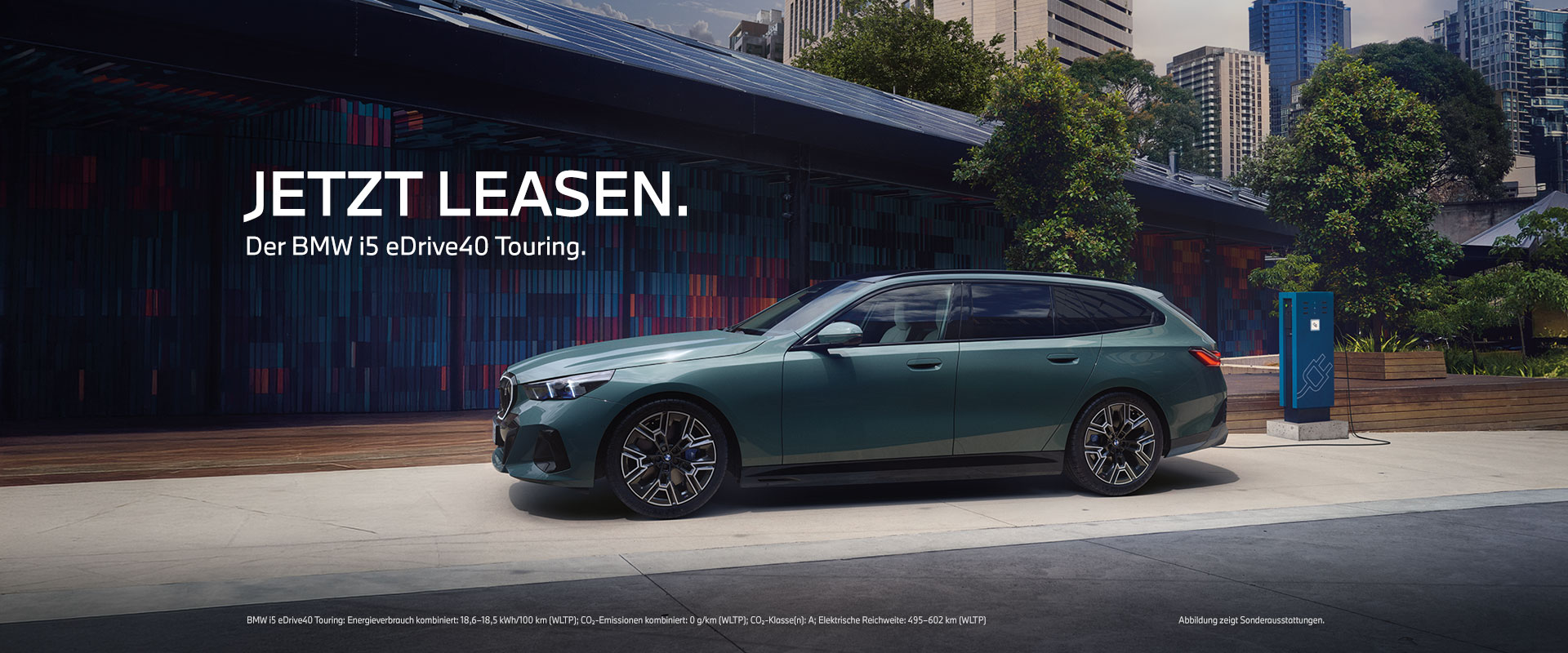 BMW i5 eDrive40 Touring – Leasing Grüner BMW i5 Touring in Seitenansicht vor einer modernen Fassade und einer Ladesäule; eingeblendet ist „Jetzt leasen“.