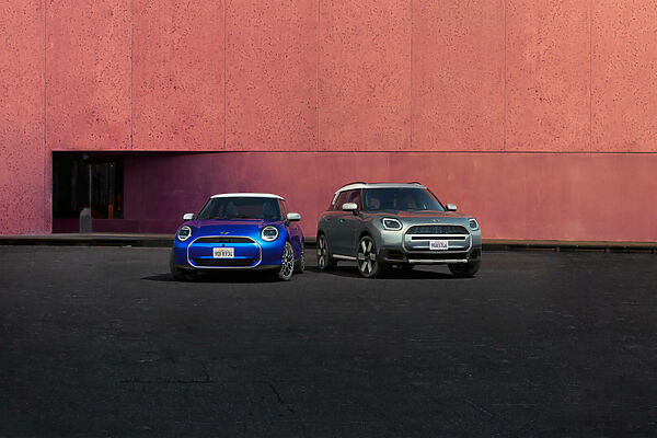 MINI Modellvielfalt Blauer MINI Cooper und grüner MINI Countryman vor einer roten Gebäudefassade.