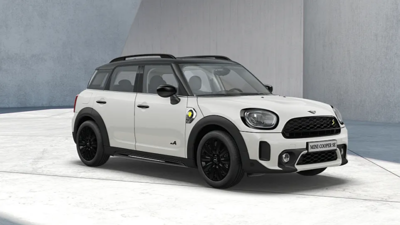 Weißer MINI Countryman mit schwarzem Dach und gelben Hybrid-Akzenten Weißer MINI Countryman mit schwarzem Dach und gelben Hybrid-Akzenten, schräg von vorn vor einer grauen Wand.
