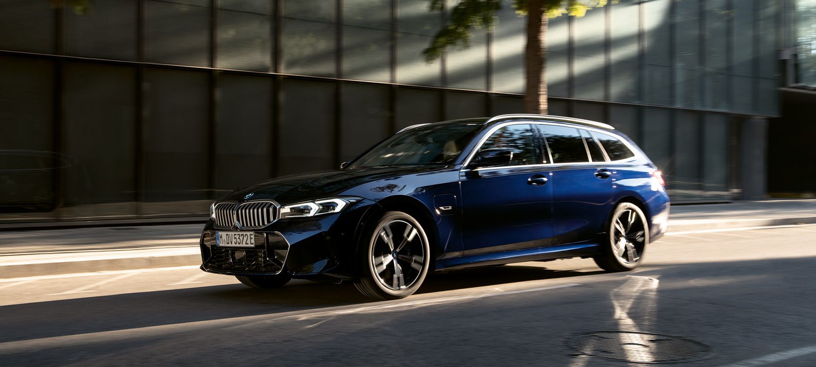 Blauer BMW 3er Touring fährt an einer modernen Gebäudefassade vorbei Blauer BMW 3er Touring fährt an einer modernen Gebäudefassade vorbei.