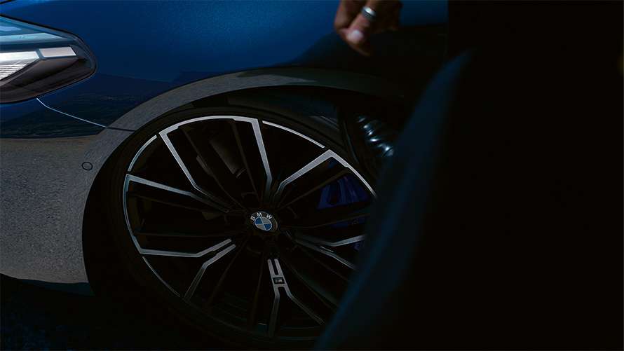 Nahaufnahme eines dunklen Leichtmetallrades an einer blauen BMW 5er Limousine Nahaufnahme eines dunklen Leichtmetallrades an einer blauen BMW 5er Limousine.