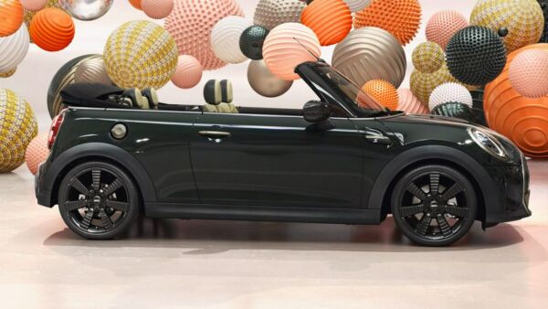 Dunkelgrünes MINI Cabrio mit geöffnetem Dach in Seitenansicht vor bunten Kugeln Dunkelgrünes MINI Cabrio mit geöffnetem Dach in Seitenansicht vor bunten Kugeln.