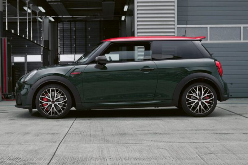 Dunkelgrüner MINI John Cooper Works mit rotem Dach vor einem Industriegebäude.