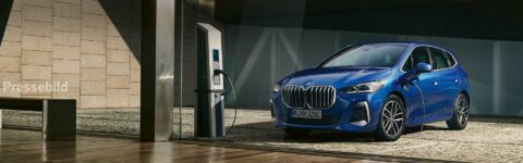 Blauer BMW Kompaktwagen vor einem modernen Gebäude mit großer Glasfassade.