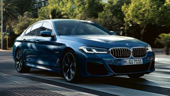 Blaue BMW 5er Limousine fährt auf einer von Bäumen gesäumten Straße Blaue BMW 5er Limousine fährt auf einer von Bäumen gesäumten Straße.