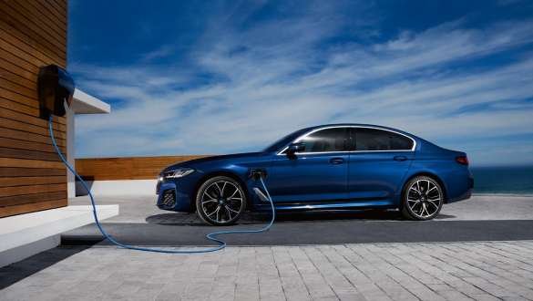 Blaue BMW 5er Limousine mit angeschlossenem Ladekabel vor einer Blaue BMW 5er Limousine mit angeschlossenem Ladekabel vor einer Ladestation an einem Haus.