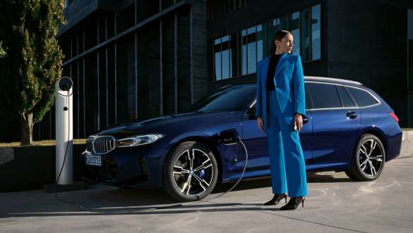 Frau steht neben einem blauen BMW 3er Touring mit angeschlossenem Ladekabel Eine Frau steht neben einem blauen BMW 3er Touring mit angeschlossenem Ladekabel.