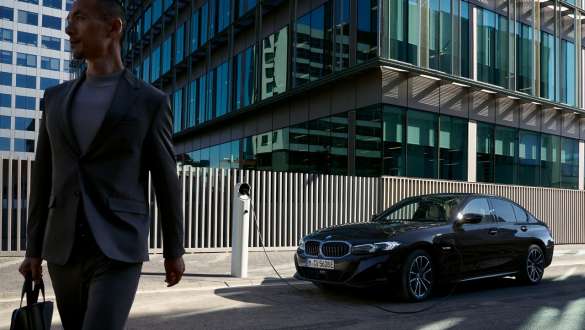 Mann geht vor einer dunklen BMW 3er Limousine an einem modernen Glasgebäude vorbei Ein Mann geht vor einer dunklen BMW 3er Limousine an einem modernen Glasgebäude vorbei.