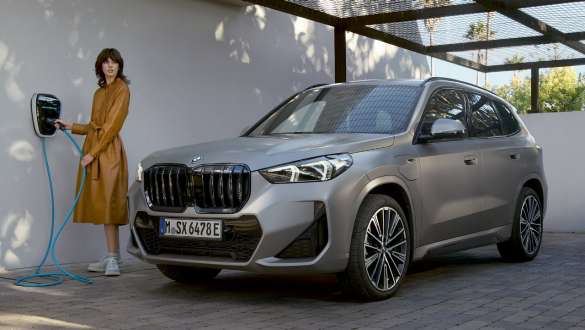 Frau steht an einer Wallbox neben einem grauen BMW Eine Frau steht an einer Wallbox neben einem grauen BMW X1 mit angeschlossenem Ladekabel.