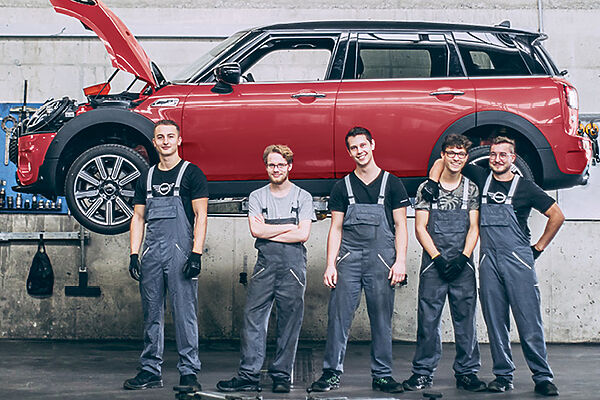 MINI Service – Werkstattteam Fünf Werkstattmitarbeiter vor einem roten MINI auf einer Hebebühne.