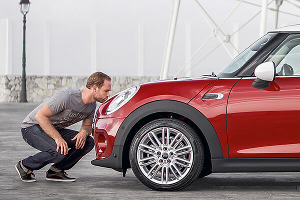 MINI Service – Fahrzeug-Check Mann prüft die Frontpartie eines roten MINI mit geöffneter Motorhaube.